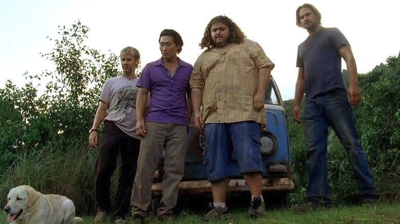 Dominic Monaghan as Charlie Pace standing in front of a Volkswagen van in a jungle next to Daniel Dae Kim as Jin-Soo Kwon, Jorge Garcia as Hugo Reyes, and Josh Holloway as James Ford in Lost