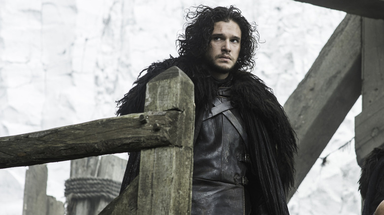 Kit Harington as Jon Snow standing on a wooden platform in front of a wall of ice in Game of Thrones
