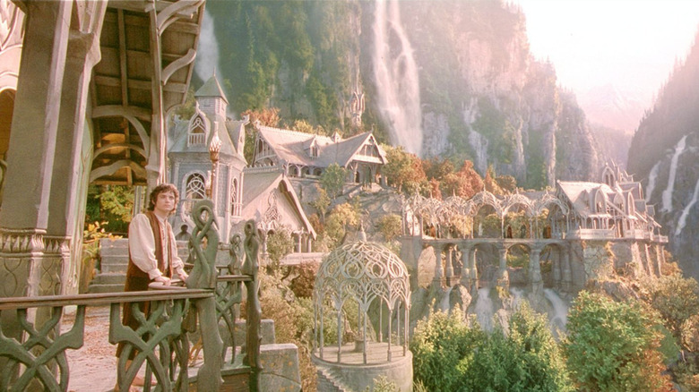 Elijah Wood as Frodo Baggins standing against a railing overlooking a valley filled with buildings and waterfalls in The Lord of the Rings: The Fellowship of the Ring