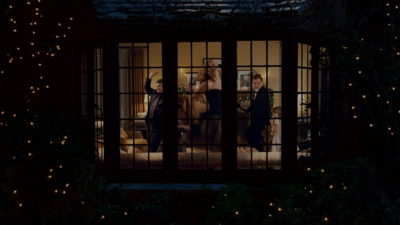 Miles Dumont, de Jack Black, Amanda Woods, de Cameron Diaz, e Graham Simpkins, de Jude Law, podem ser vistos através de uma janela dançando dentro de uma sala de estar aconchegante em The Holiday