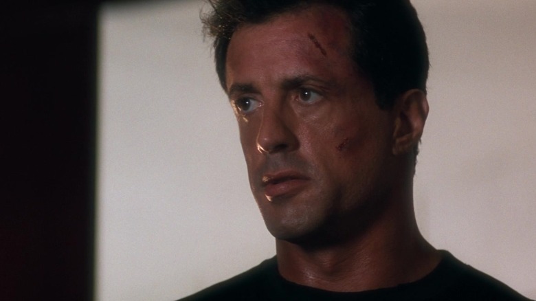 Sylvester Stallone's John Spartan stands against a white background with a cut on his forehead in Demolition Man