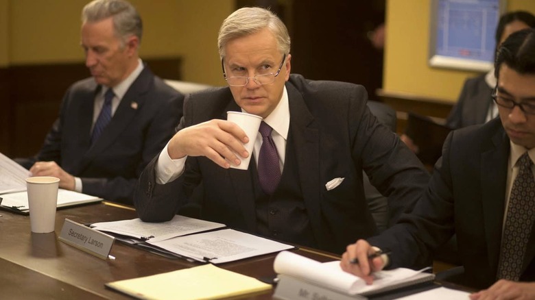 Tim Robbins as Walter Larson drinking coffee in a board room in The Brink