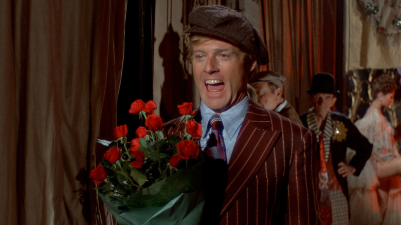 Robert Redford como Johnny Hooker, parecendo animado com flores nos bastidores da picada