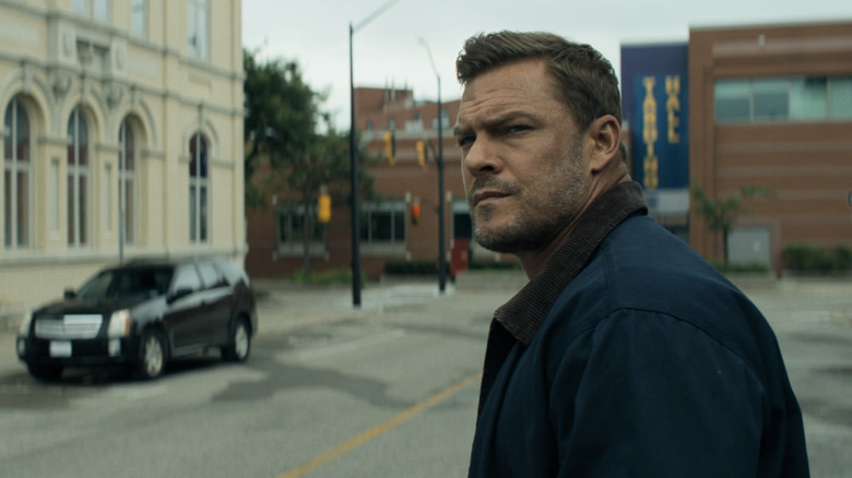 Alan Ritchson's Jack Reacher stands in a street looking to his left in Reacher