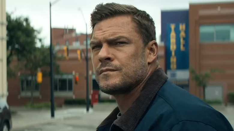 Alan Ritchson as Jack Reacher standing near a street in Reacher