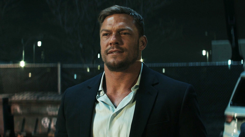 Alan Ritchson as Jack Reacher stands outside in a suit in Reacher