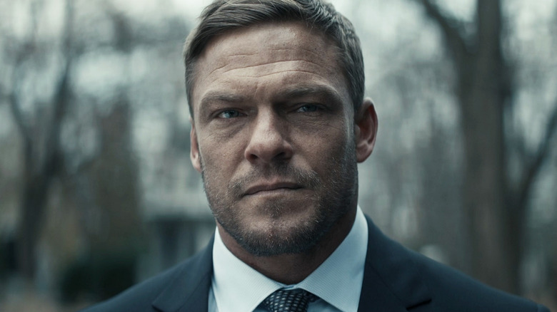 Alan RItchson as Jack Reacher standing wearing a suit in Reacher