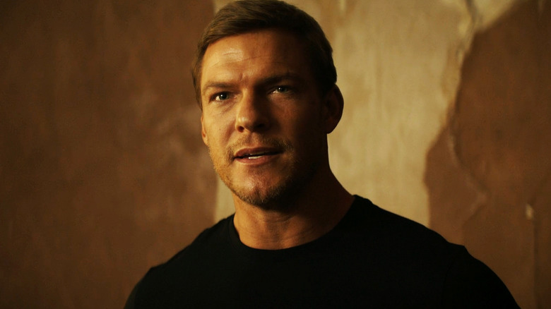 Alan RItchson's Jack Reacher is seen in closeup against an orange wall in Reacher