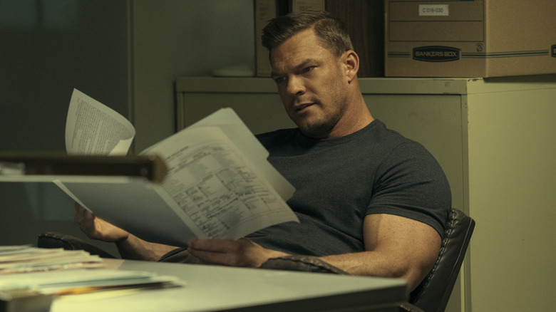 Alan Ritchson as Reacher reading a document while sat at a desk