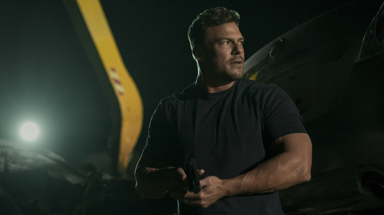 Alan Ritchson as Reacher holding a pistol