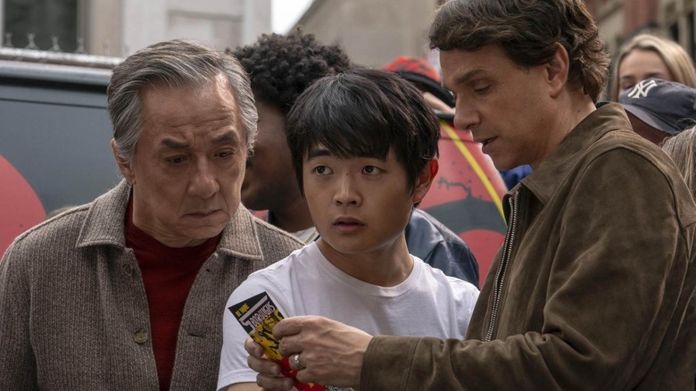 Han and Daniel looking at a flyer, while Li looks forward in Karate Kid: Legends