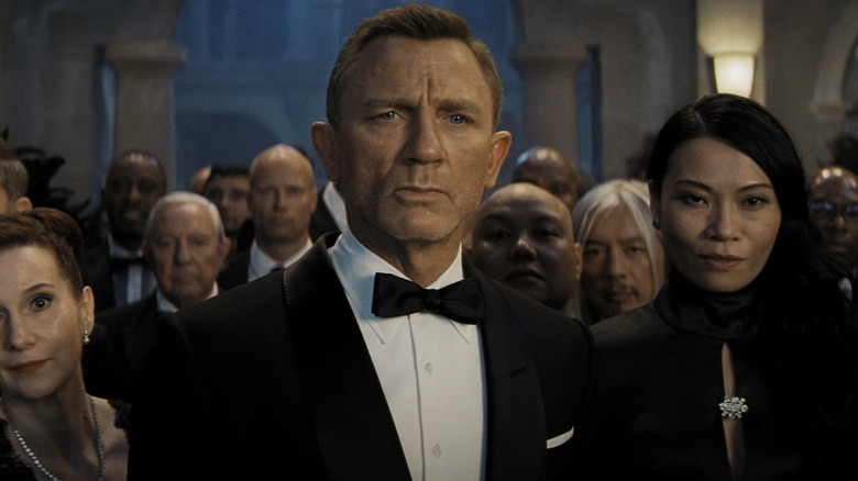 Daniel Craig's James Bond is seen standing among a crowd in closeup in No Time to Die