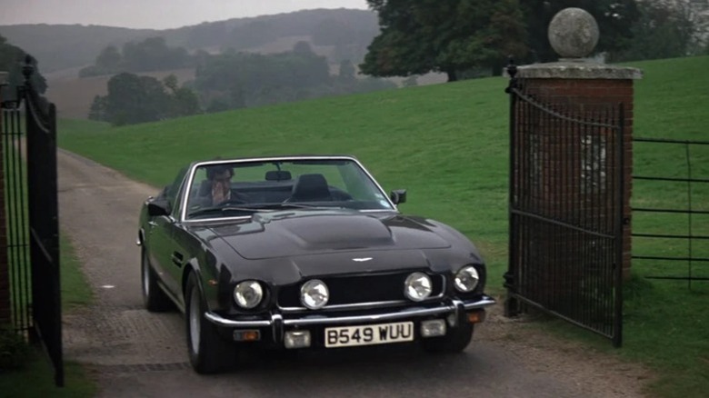 Timothy Dalton as James Bond driving the 1985 Aston Martin V8 Vantage as it pulls into a driveway with open gates in The Living Daylights