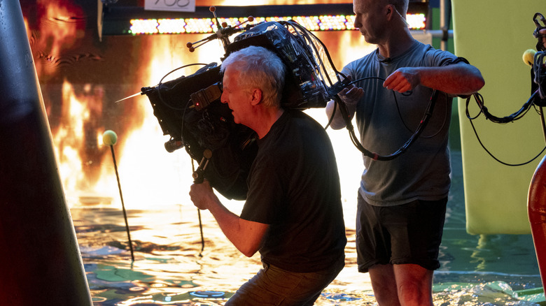 Director James Cameron filming an action scene in a water tank with a wall of flames in the background in a behind-the-scenes still from Avatar: The Way of Water