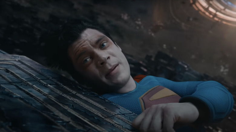 David Corenswet as Superman looks down while laying on a rock in Superman