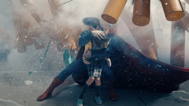 Superman protects a little girl from an explosion, shielding her with his body and cape, in Superman