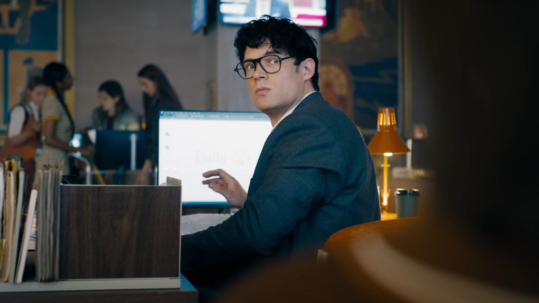 Clark Kent, in disguise at his desk at the Daily Bugle with glasses and a suit, looks over his shoulder in Superman