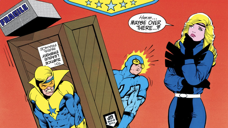 Justice League International #8 Portada: Blue Beetle y Booster Gold que transportan una caja pesada como Black Canary considera dónde ponerlo