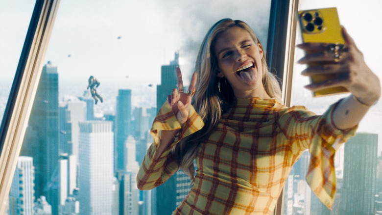 Eve Teschmacher takes a personal photo in the Luthorcorp building with Superman fighting in the background in Superman