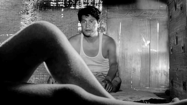 Niki Junpei (Eiji Okada) sits in a hut looking at a woman's bare legs in Woman in the Dunes