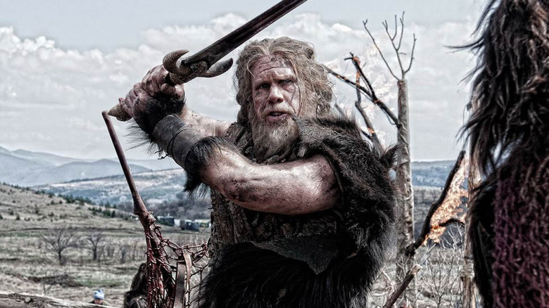 Ron Perlman as Corin holding his sword overhead in Conan the Barbarian (2011)