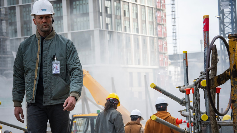 Jason Statham as Levon Cade wearing a hardhat and walking through a construction zone in A Working Man