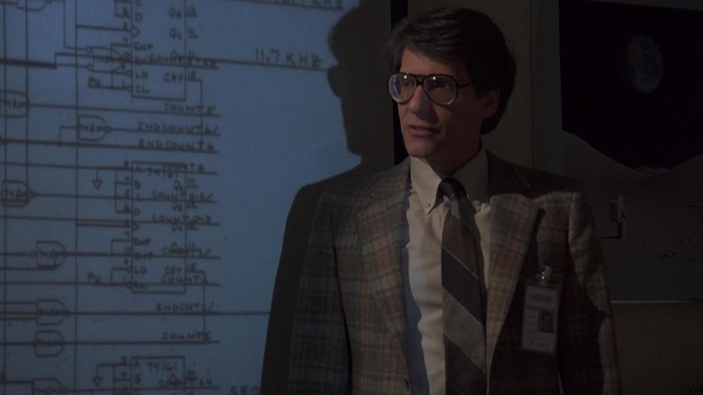 David Cronenberg as a group supervisor standing in front of a projected image in Into the Night