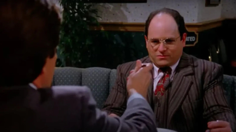 George, sitting at a table, refusing to eat a bite of food that is being offered to him. A scene from Seinfeld.