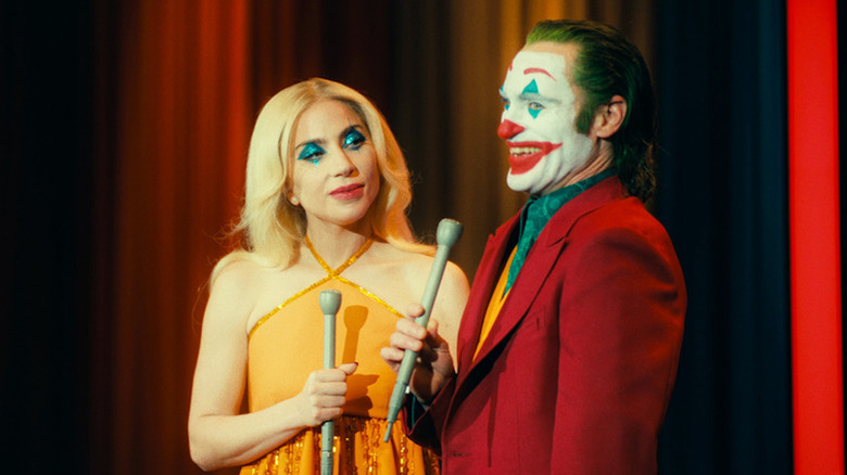 Joaquin Phoenix sorri como Arthur Fleck ao lado de Lady Gaga como Lee Quinzel em Joker Folie a Deux