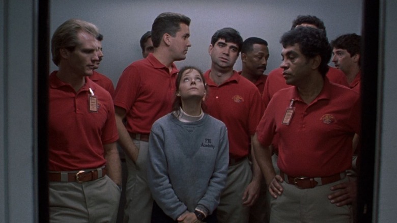 Jodie Foster as Clarice Starling in The Silence of the Lambs standing in the FBI elevator surrounding by male agents in red shirts