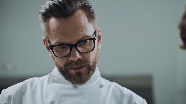 Chef David (Joel McChelil) wears glasses and white chefs, looks down with a wise expression in the bear