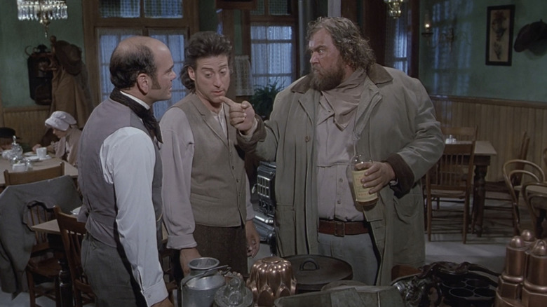 रिचर्ड लुईसचा फिल टेलर रॉबर्ट पिकार्डोच्या बेन व्हीलरच्या बाजूला उभा आहे कारण जॉन कँडीचा जेम्स हार्लो वॅगन्स ईस्टमध्ये त्यांच्या चेहऱ्यावर बोट दाखवतो!