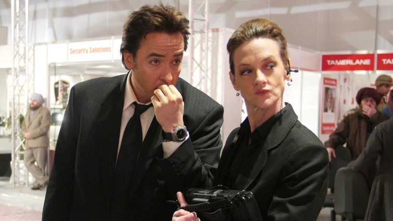John Cusack as Brand Hauser and Joan Cusack as Marsha Dillon dressed all in black at an arms convention in War, Inc.