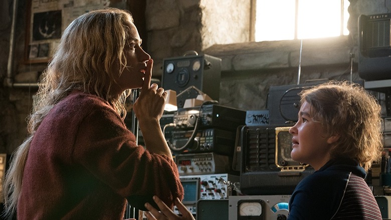 Emily Blunt como Evelyn sinalizando para Millicent Simmonds como Regan para ficar quieto no porão em um lugar tranquilo