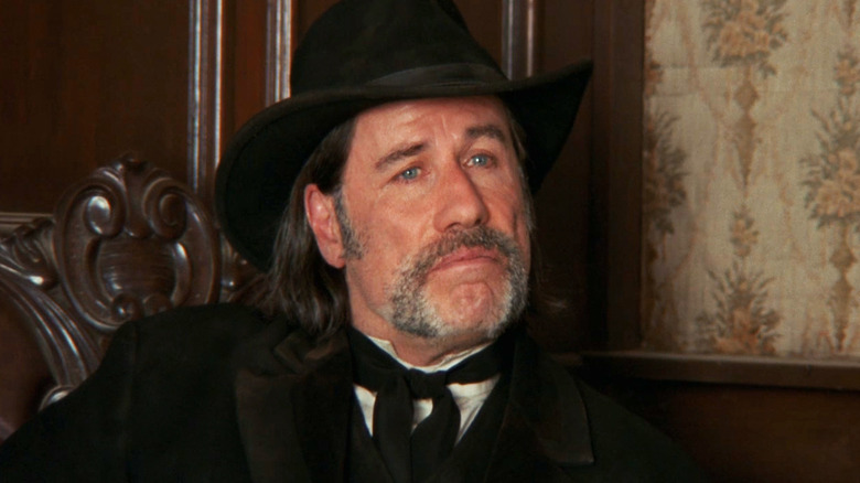 John Travolta's Clyde Martin looks across frame as he sits in a wooden chair in In a Valley of Violence