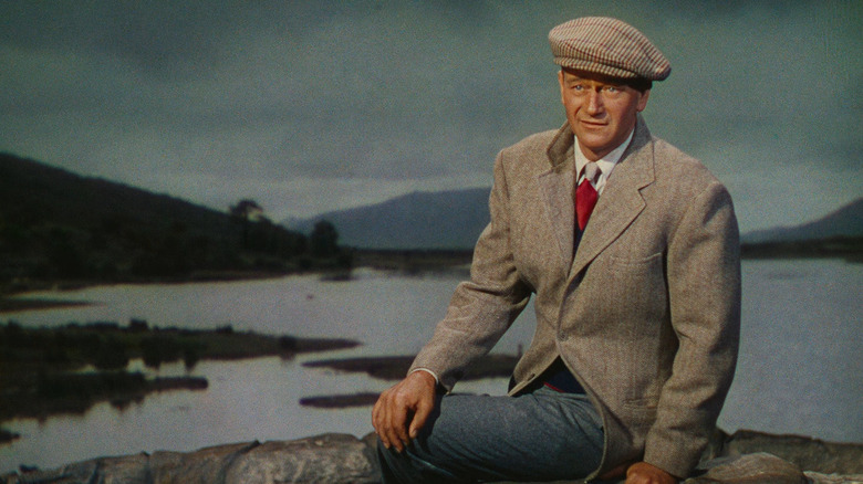 John Wayne as Sean Thornton sitting near a lake in The Quiet man