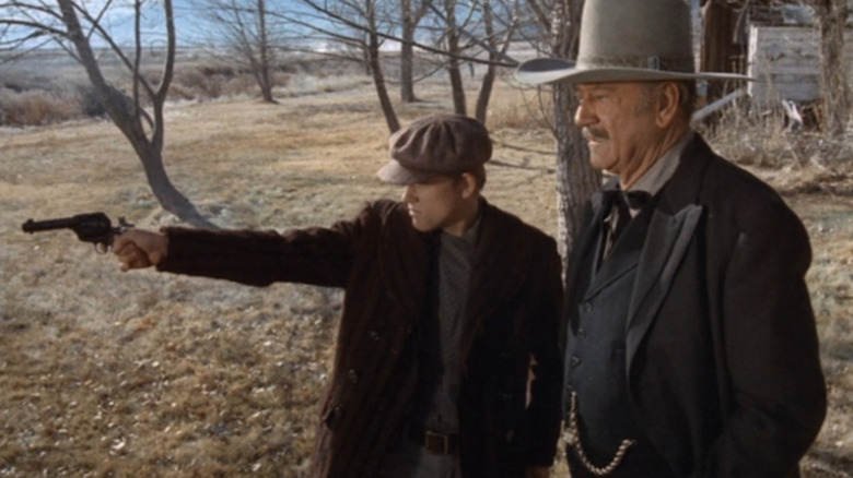 John Wayne's J B Books stands next to Ron Howard's Gillom Rogers as he shoots a pistol in The Shootist