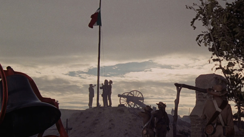Soldiers raise a flag against a  twilight sky in The Alamo