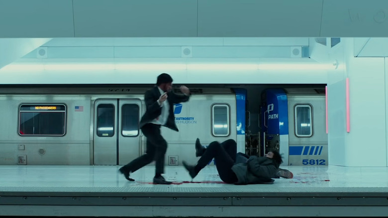John Wick leaning over a man who's bleeding between the legs in the subway