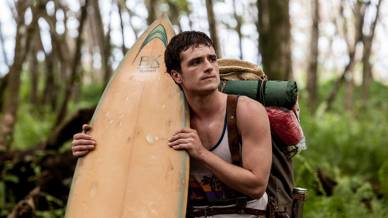 Nick holding his surfboard and looking around in Escobar: Paradise Lost