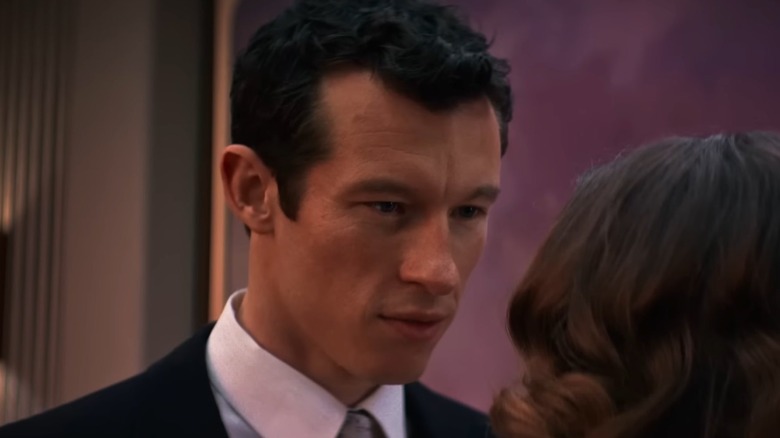 Callum Turner as Luke wearing a suit and tie and looking intently at Elizabeth Olsen as Joan in Eternity