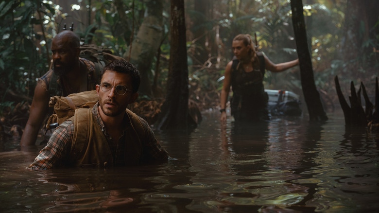 Bechir Sylvain as Leclerc, Jonathan Bailey as Dr. Henry Loomis, and Scarlett Johansson as Zora Bennett wading through a swamp in Jurassic World Rebirth