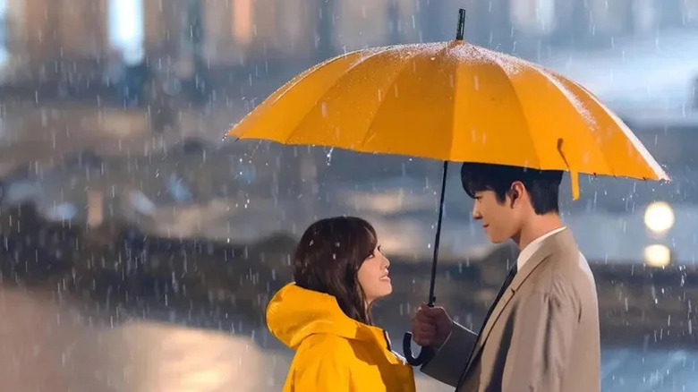 Kang Tae-moo (Ahn Hyo-seop) shelters Shin Ha-ri (Kim Se-jeong) under his yellow umbrella in the rain in Business Proposal