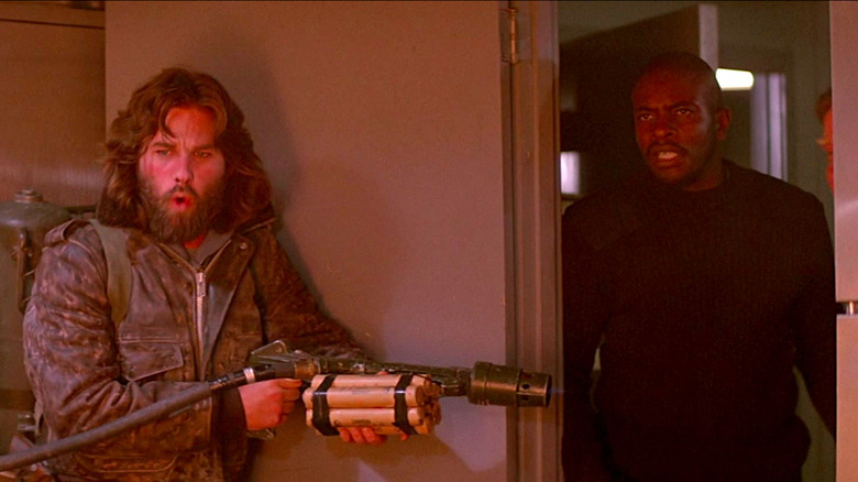 Kurt Russell holds a flamethrower while Keith David stands in the doorway in The Thing