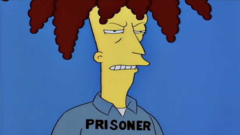Sideshow Bob looks angry as he stands against a blue background and wears a suit that reads Prisoner in The Simpsons