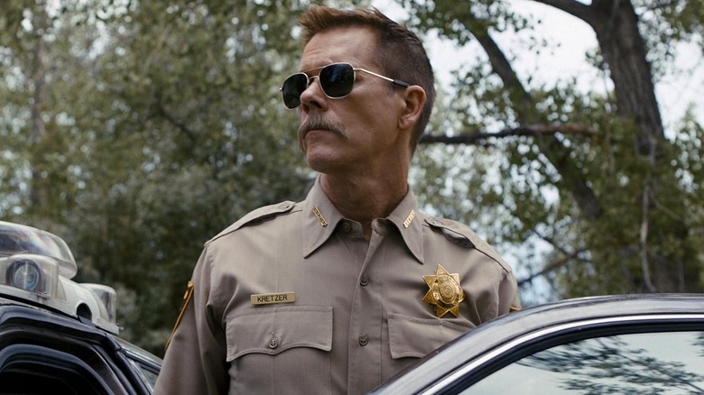 కెవిన్ బేకన్ కాప్ కార్‌లో షెరీఫ్ క్రెట్జర్‌గా కాప్ సన్ గ్లాసెస్ మరియు కాప్ మీసం