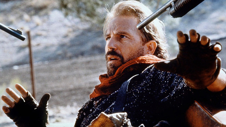 Kevin Costner as the Postman on his knees with guns in his face in The Postman