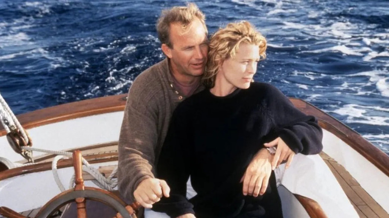 Garret (Kevin Costner) sits behind Theresa (Robin Wright), one arm around her waist and the other holding on a sailboat's steering wheel, in the middle of the ocean in a scene from Message in a Bottle