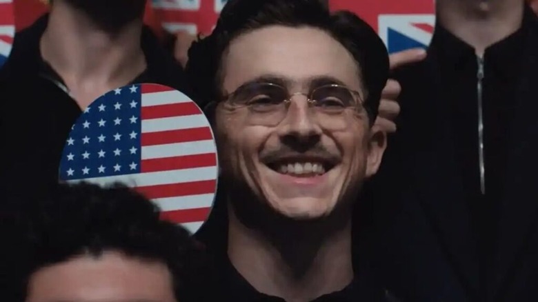 Marty Mauser holding up an American flag ping pong paddle in Marty Supreme