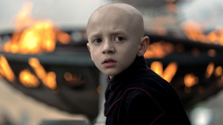 Dexter Sol Ansell as Egg dressed all in black and standing in front of a brazier filled with flames in A Knight of the Seven Kingdoms